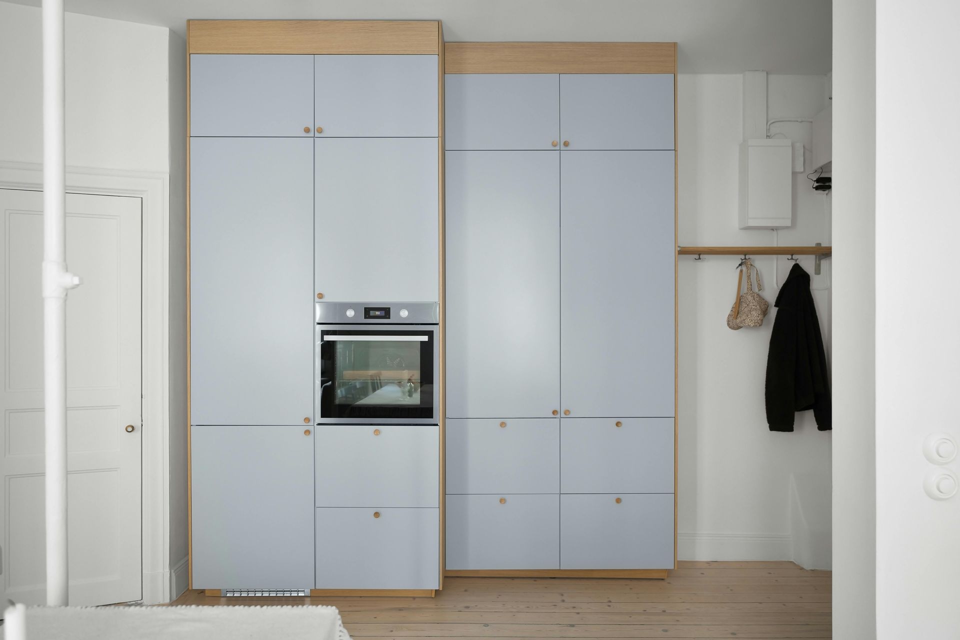 Pale blue floor to ceiling pantry cabinets with oak trim and an integrated oven