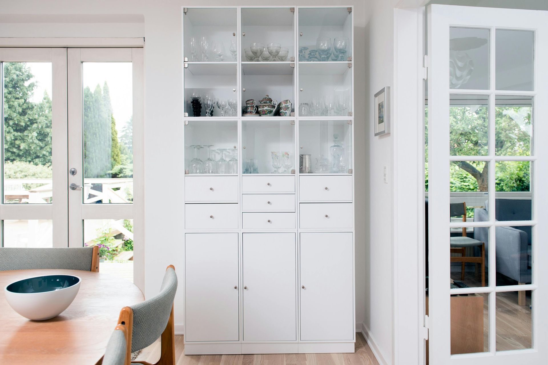Floor to ceiling white display cabinetry with glass fronts beside a dining table