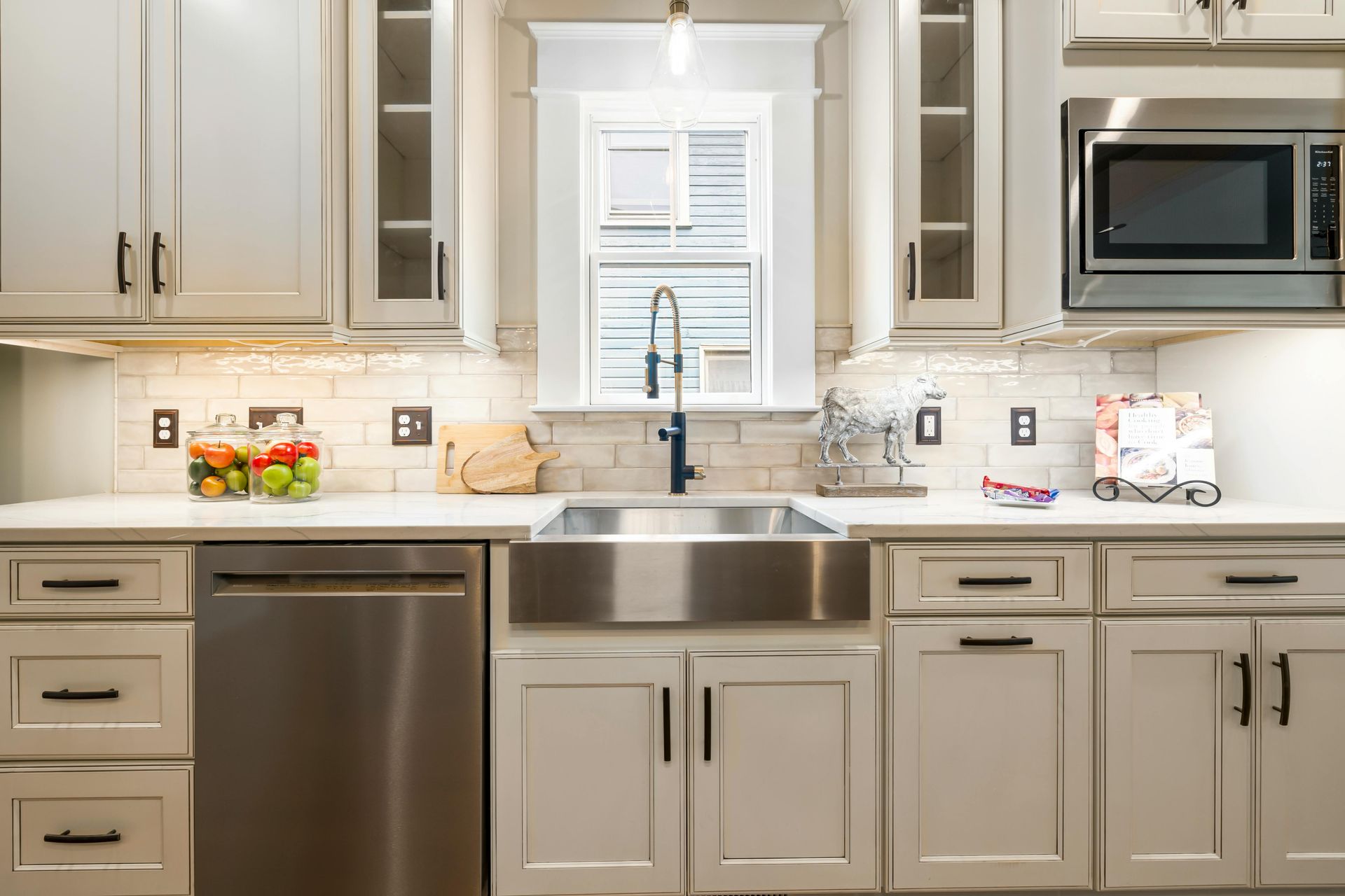 Greige kitchen cabinets with a stainless farmhouse sink and glass fronted display cabinets